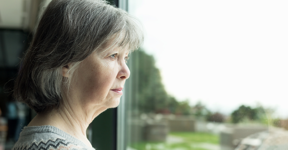 Older woman feeling lonely whilst starting out the window
